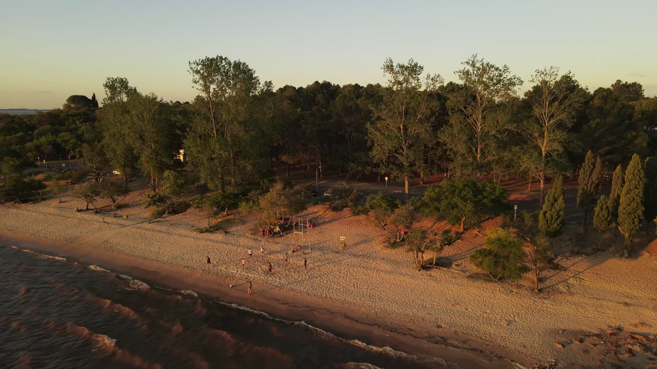 vista aérea: grupo de amigos jugando voleibol en la playa de arena durante la hora dorada