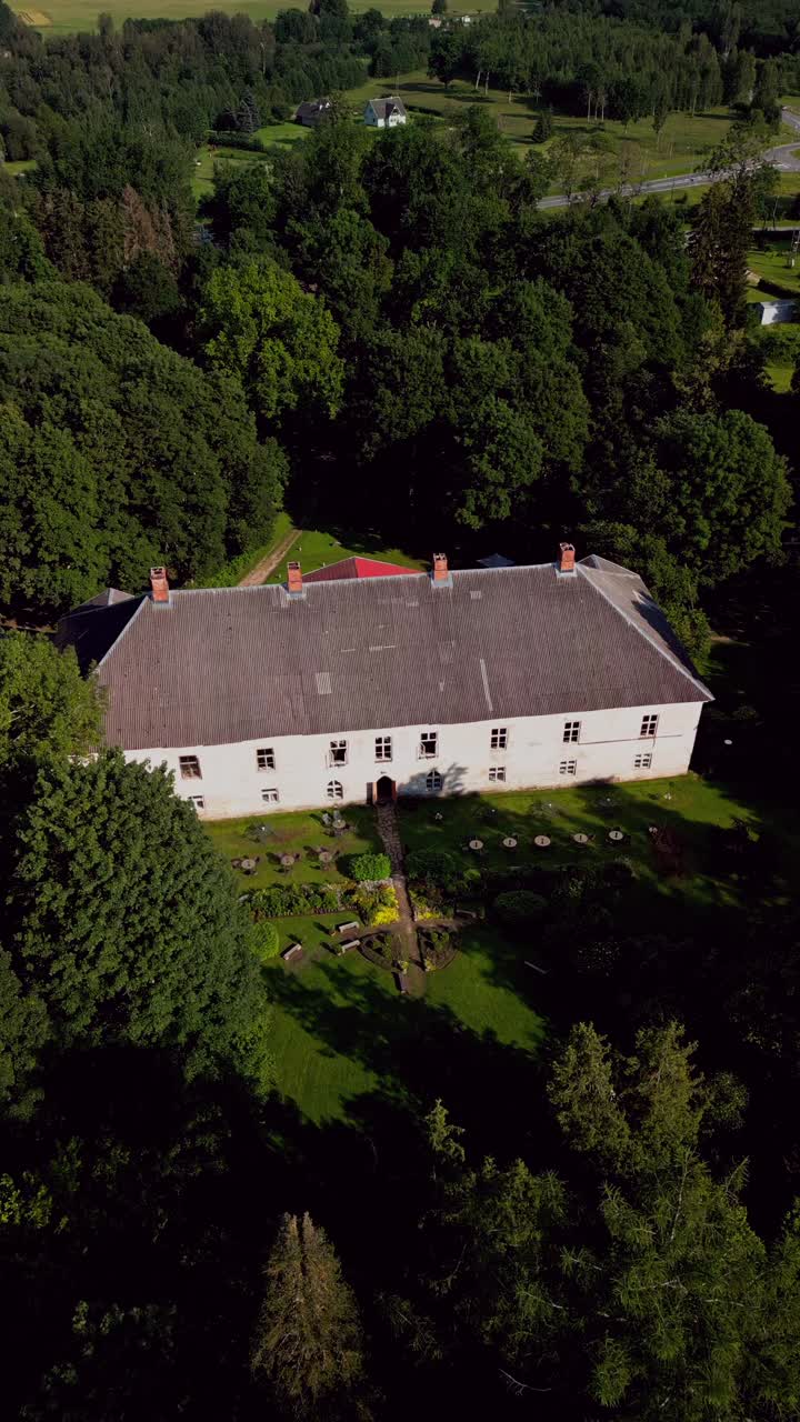 Vertical drone footage captures the serene beauty of Kirna Manor surrounded by green landscapes offering a peaceful view of this historic Estonian estate on a sunny day