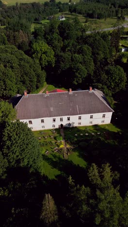 Vertical drone footage captures the serene beauty of Kirna Manor surrounded by green landscapes offering a peaceful view of this historic Estonian estate on a sunny day