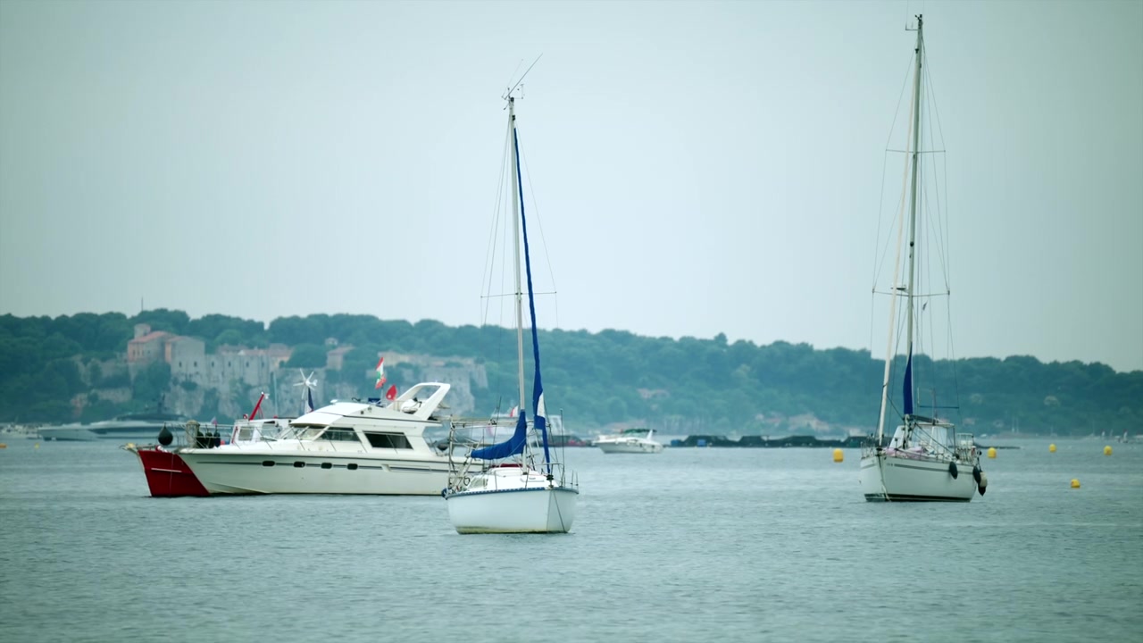 Des yachts et des voiliers sur une eau calme avec un bâtiment historique sur le littoral boisé de la Côte d'Azur à Cannes, Antibes, France.