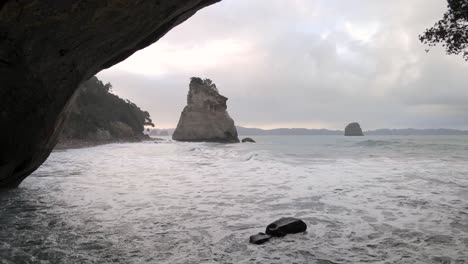 unique aerial pull back from standing rock formation throught cave at cathedral cove, new zealand