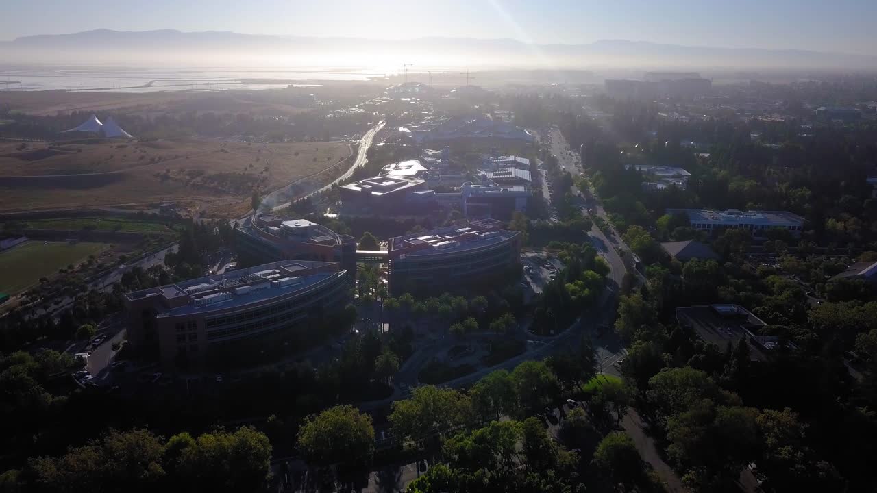 Aerial drone view of Google campus called googleplex headquarters in silicon valley flying forward early morning sunrays glaring on solar panels on rooftop