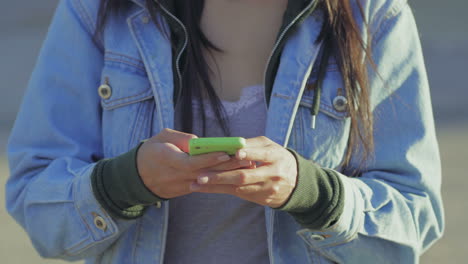 una foto recortada de una chica usando un teléfono inteligente mientras camina.