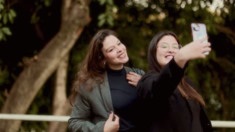 two women enjoying time together, taking selfies and interacting with a smartphone in a park