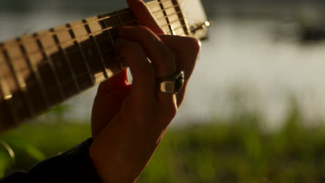 close-up of a person playing an acoustic guitar by a river