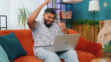 amazed indian man use laptop computer, receive good news message, shocked by victory, celebrate win