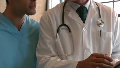 médico serio hablando con una enfermera masculina mientras sostiene una tableta