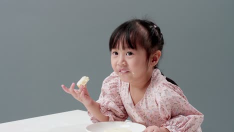 asiatic child eating piece of sweet in the studio with a gray background