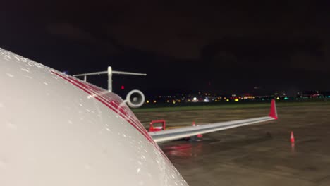 vista nocturna de la parte superior del fuselaje de un jet en una noche lluviosa y fría con otros tráficos en el aeropuerto