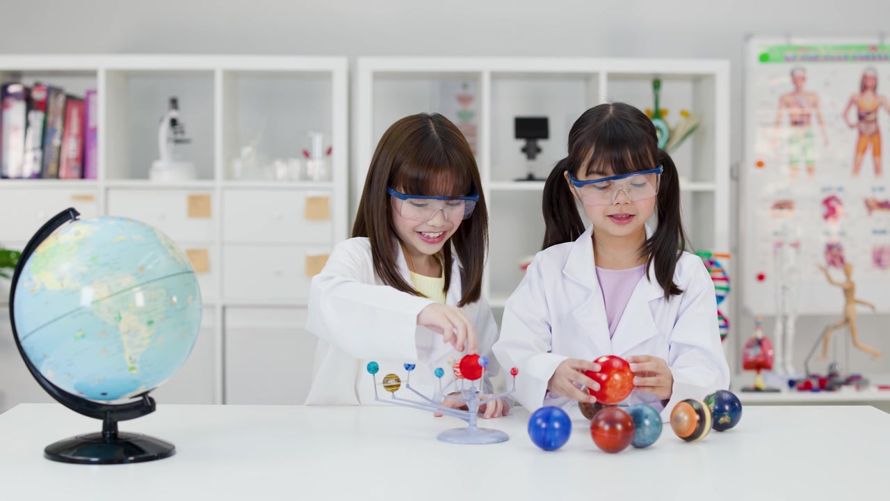 Two young students in safety goggles examine a planetary model during a science lesson.