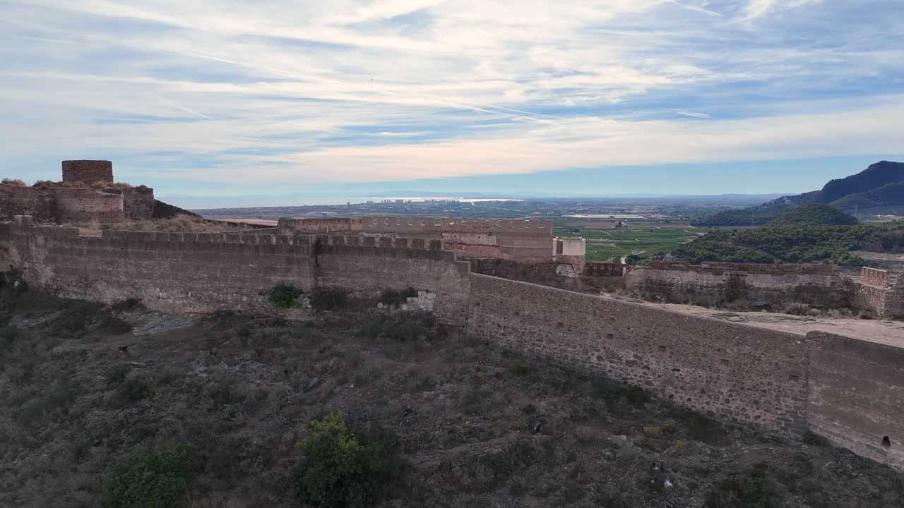vuelo de avión no tripulado con imágenes de alta calidad visualizando la fortaleza en la colina con sus imponentes muros y un fondo de montañas con un cielo azul con nubes blancas en invierno en valencia, españa