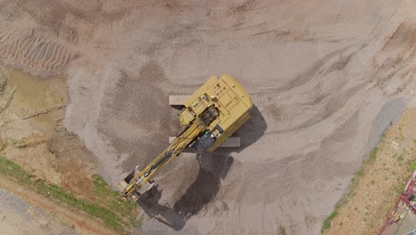 top down aerial of a digger or excavator moving around aggrated or gravel