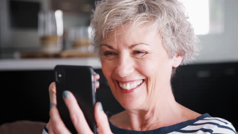 senior woman video calling on smartphone at home, close up