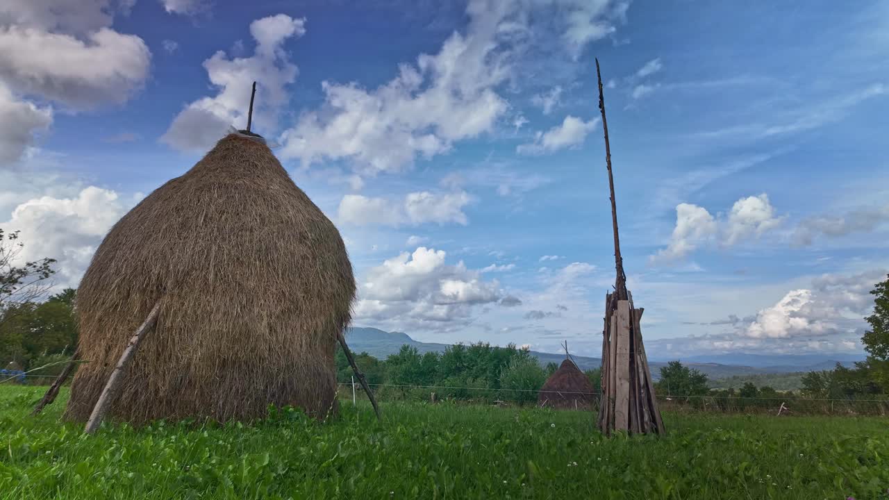 Clouds move over Romanian rural farm landscape with cows and haystacks