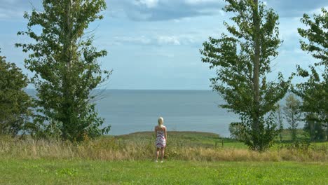 Eine-Frau,-Die-Auf-Einer-Landzunge-Steht-Und-Auf-Das-Meer-Und-Den-Bewölkten-Himmel-Blickt,-Umgeben-Von-Viel-Grün