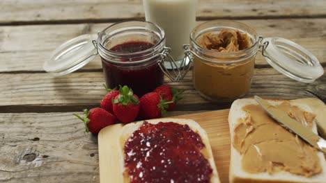 sándwich de mantequilla de maní y jalea en una bandeja de madera con leche y fresas en una superficie de madera