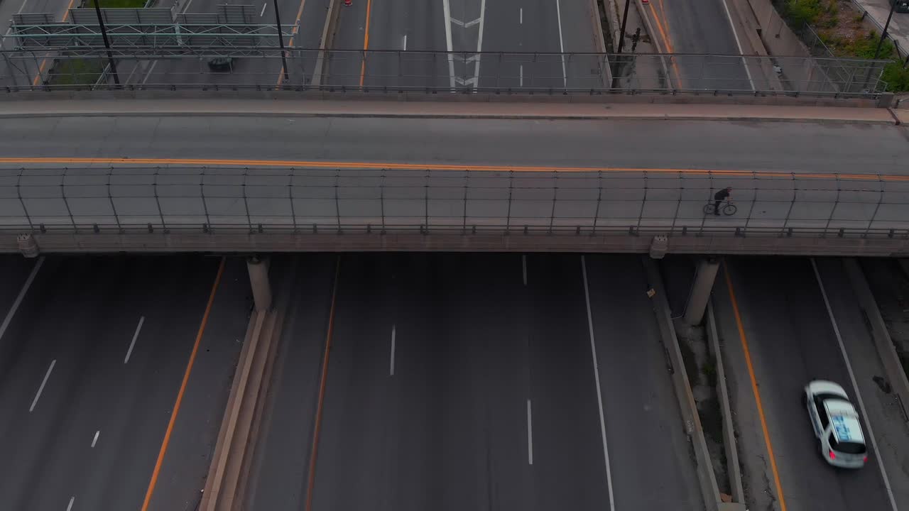 Moving vehicular traffic on six-lane highway with on and off ramps under bridge overhead, descending aerial