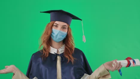 educación a distancia estudiante adulta de sexo femenino con máscara médica y una túnica académica y sombrero con diploma extiende los brazos a los lados sobre un fondo verde