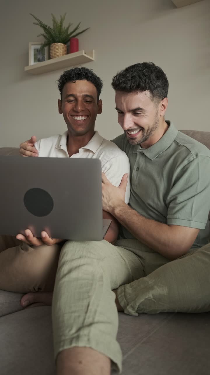 Two men laughing while using a laptop on the couch