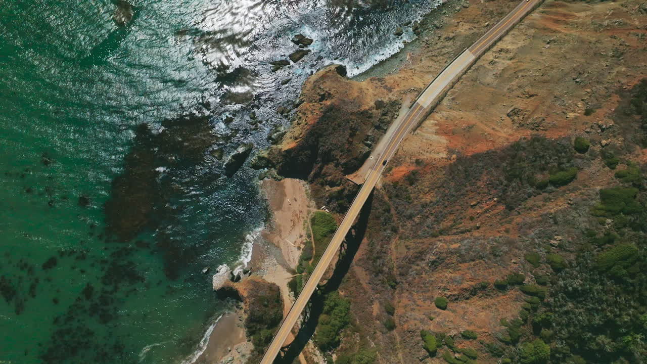 View of the roads in the mountains connected by the bridge. Rocky coastline of California with beautiful blue ocean from aerial perspective.