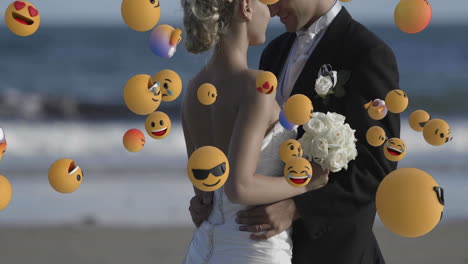 animation of emoji icons over happy caucasian married couple embracing at beach