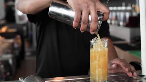 cóctel de naranja que se vierte sobre cubitos de hielo en un vaso alto en cámara lenta