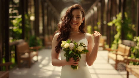 cheerful bride posing with bouquet under arch