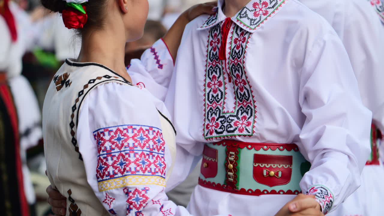 Bailarines con trajes tradicionales vibrantes interpretan animadas danzas folclóricas en un festival de verano en la plaza de una comunidad, celebrando las costumbres y la cultura local con expresiones alegres. Cámara lenta