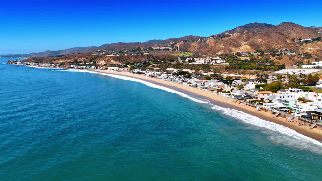 Flight along the rocky coast of Malibu, Los Angeles County, California, USA. Waves splash to the sandy beach with no people