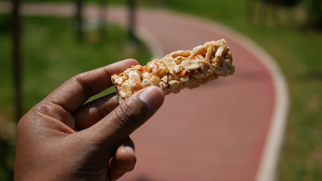 Hand Holding a Piece of Peanut Brittle in a Park