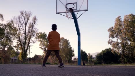 Nivel-Del-Suelo,-Vista-Baja-Del-Niño-Caucásico-Que-Intenta-Tiros-De-Baloncesto,-Pierde-El-Balón-De-Aire,-En-La-Cancha-De-Baloncesto-De-Espacio-Abierto,-árboles-En-El-Fondo