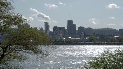 the montreal skyline and ferris wheel from across the st lawrence river on a sunny afternoon with trees in the foreground