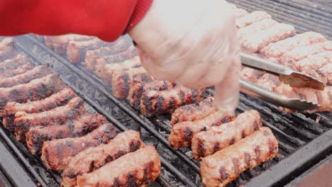 Man-hand-with-food-tongs-barbecue-turning-grill-minced-meat-rolls-while-grilling-on-charcoal-grill