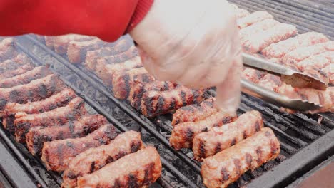 mano de hombre con pinzas para comida barbacoa girando la parrilla rollos de carne picada mientras asa en una parrilla de carbón