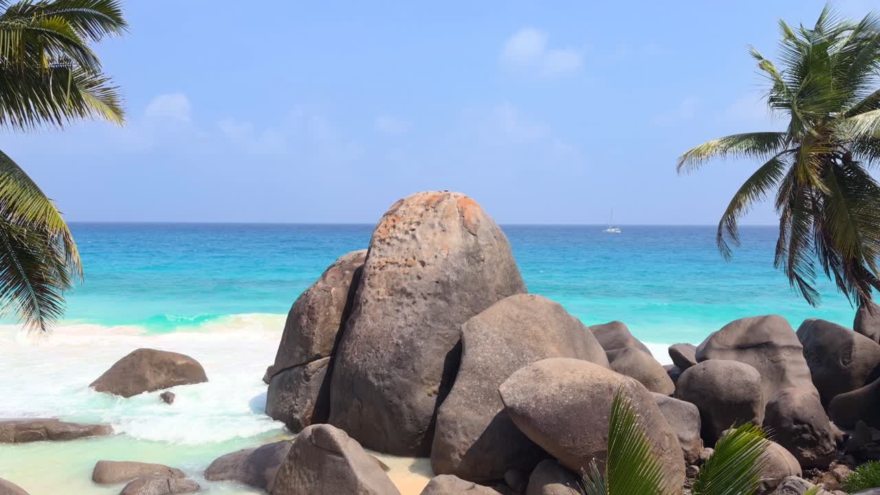 Vista mozzafiato sull'oceano, enormi pietre di granito, acqua turchese, palme da cocco e catamarano di passaggio, spiaggia di Carana, Mahe, Seychelles 30fps