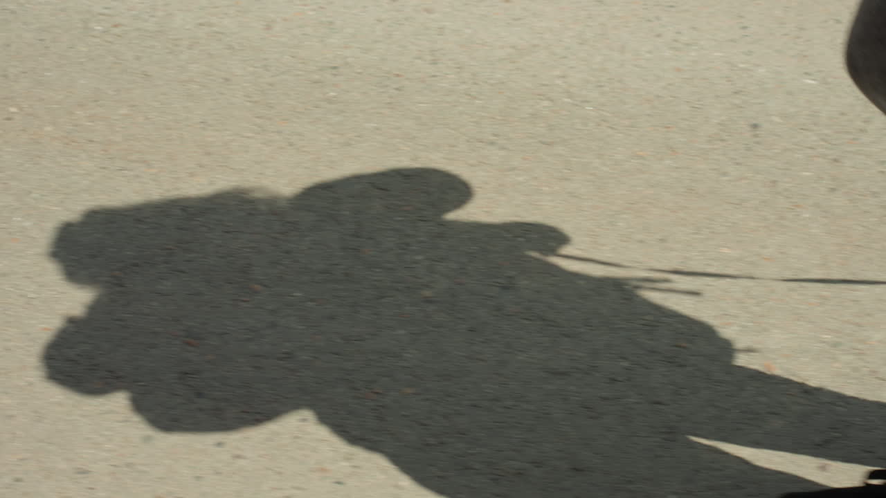Shadow Of Person With Backpack On Pavement, Elongated Silhouette Cast By Midday Sun, JeansClad Legs Stepping With Steady Rhythm, Quiet Anonymous Commute, Exploration Mood, Subtle Contrast And Texture