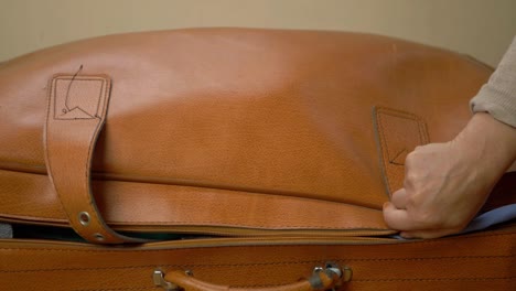 hand closing old brown suitcase with straw hat medium shot