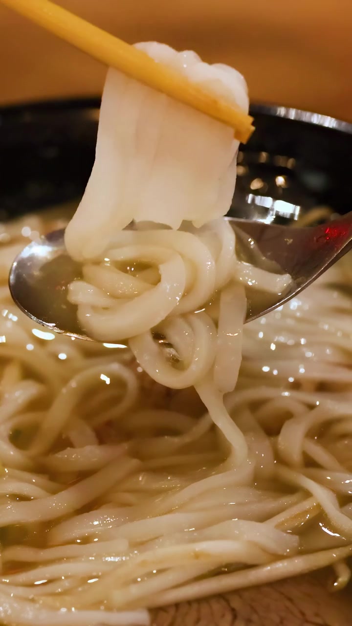 湯気の立つフォーの丼から麺が持ち上げられているクローズアップ。麺の質感と温かさが強調されている。