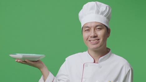 close up of asian man chef holding a dish and smiling to camera while standing in the green screen background studio