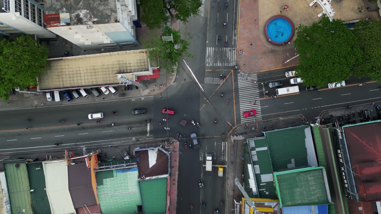 Bustling traffic with motorcycles and cars merging at a 4-way intersection along cityscape of Shoe Avenue and Sumulong Highway, Marikina City, Philippines - aerial top-down view