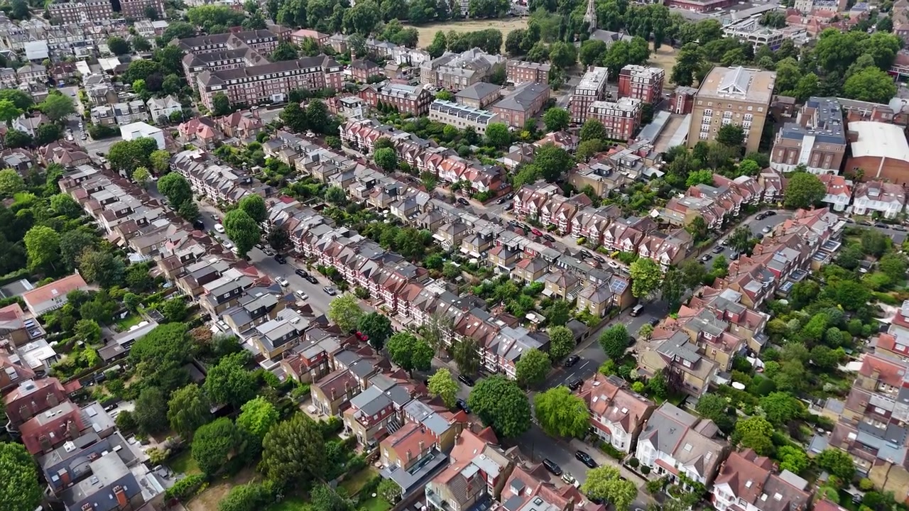 Reihen von Reihenhäusern und Hintergärten erstrecken sich in einem dicht bewachsenen Vorort im Westen Londons unter einem hellen Sommerhimmel.