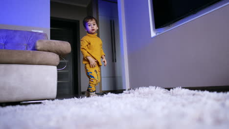 energetic caucasian toddler in yellow clothes jumping cheerfully and rolling by the floor. kid having fun at home. low angle view.