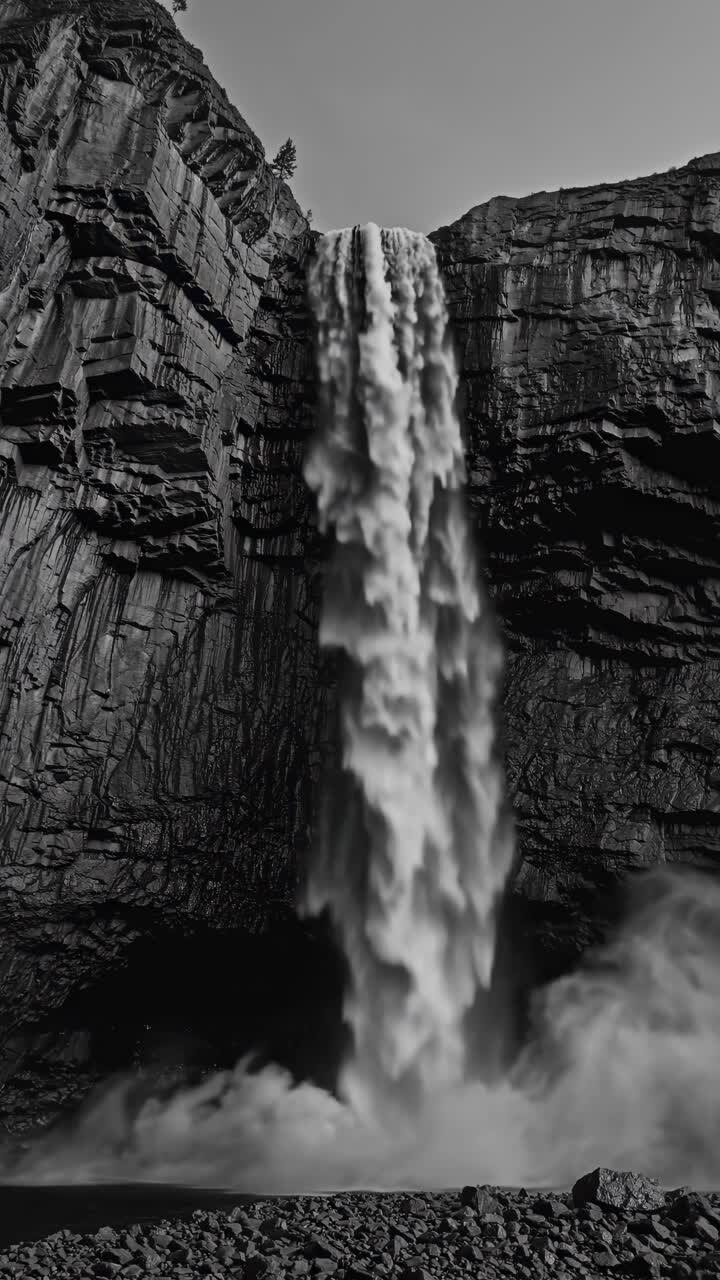 Dramatic black and white video still of a waterfall cascading down rugged cliffs