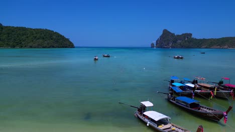 Koh-Phi-Phi-Bay,-colorful-traditional-longtail-boats-are-floating-on-calm-turquoise-water