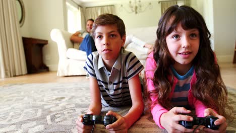 hermanos acostados en la alfombra y jugando a videojuegos