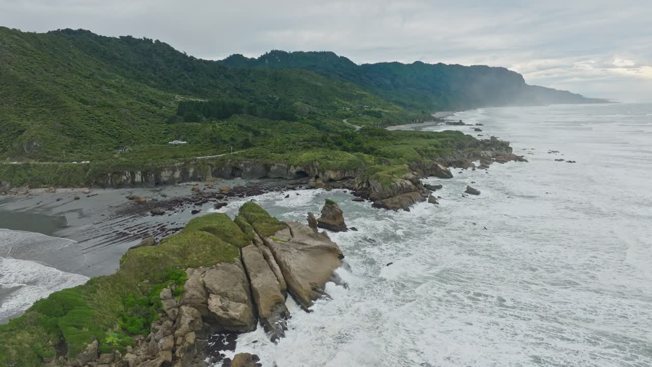Reverse aerial view of wild, rugged and remote West Coast with waves crashing into rocky shoreline on the South Island of New Zealand Aotearoa
