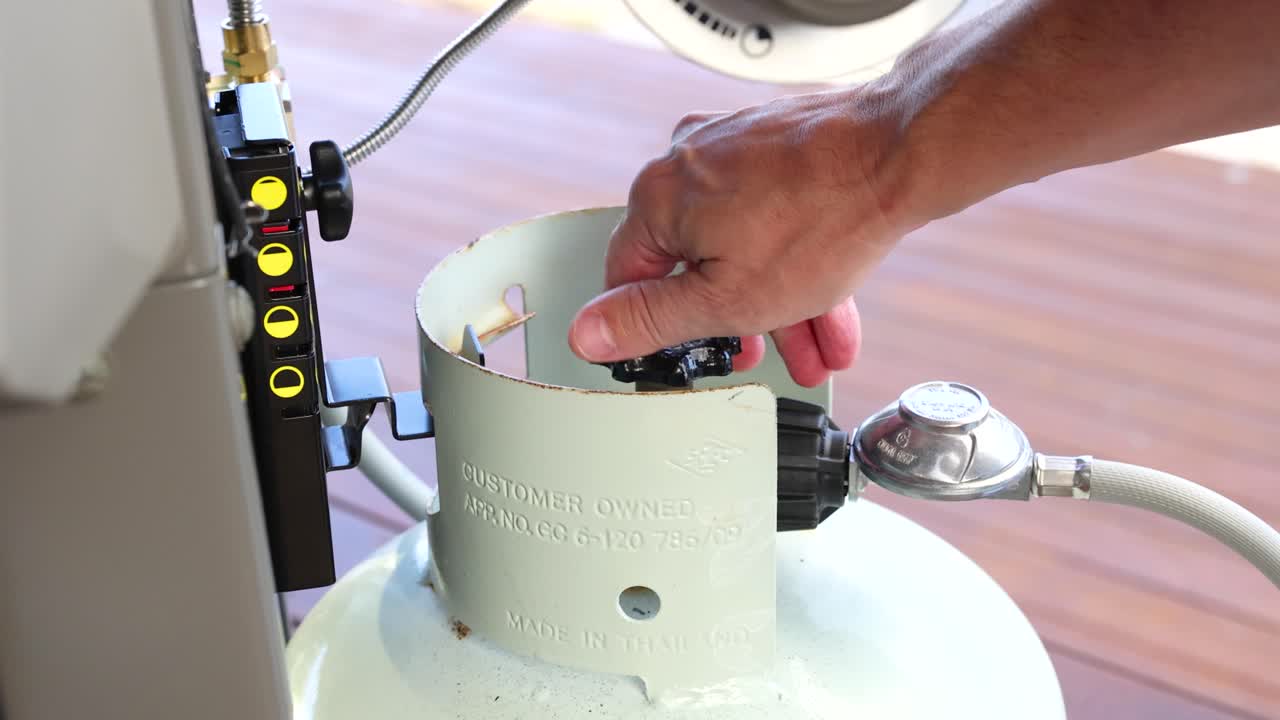 A hand turns a valve on a gas grill tank outdoors. Bright lighting highlights the action in a casual setting