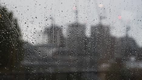 raindrops falling down on window with blurred construction cranes in background