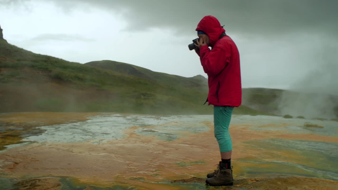 Dramatisk islandsk landskab med opstigende geotermisk damp. En person i scenen, en fotograf tager et billede med kameraet i en panorering, optaget med vidvinkelobjektiv.