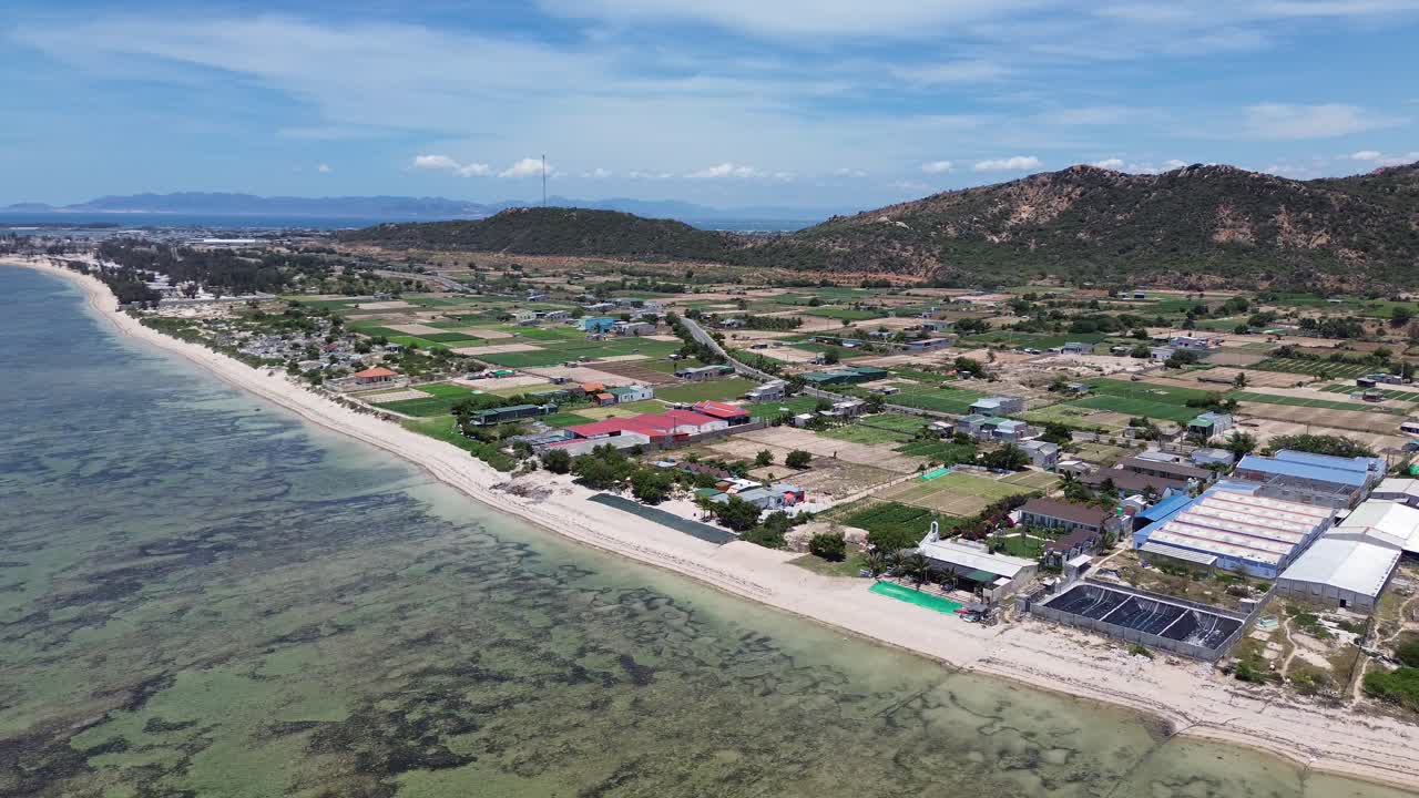 Semi orbit drone movement revealing the colorful patchwork of farmlands and My Hoa Lagoon meeting at the shore under midday sun. My Hoa Vietnam, famous kitesurfing spot during low season.
